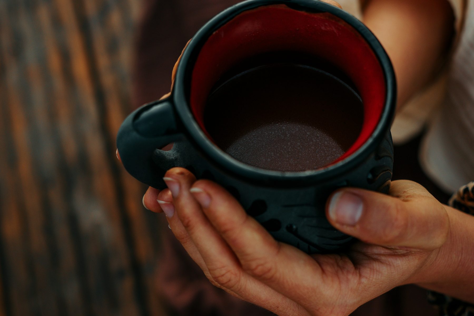 Hands cradling a clay mug of freshly whisked cacao