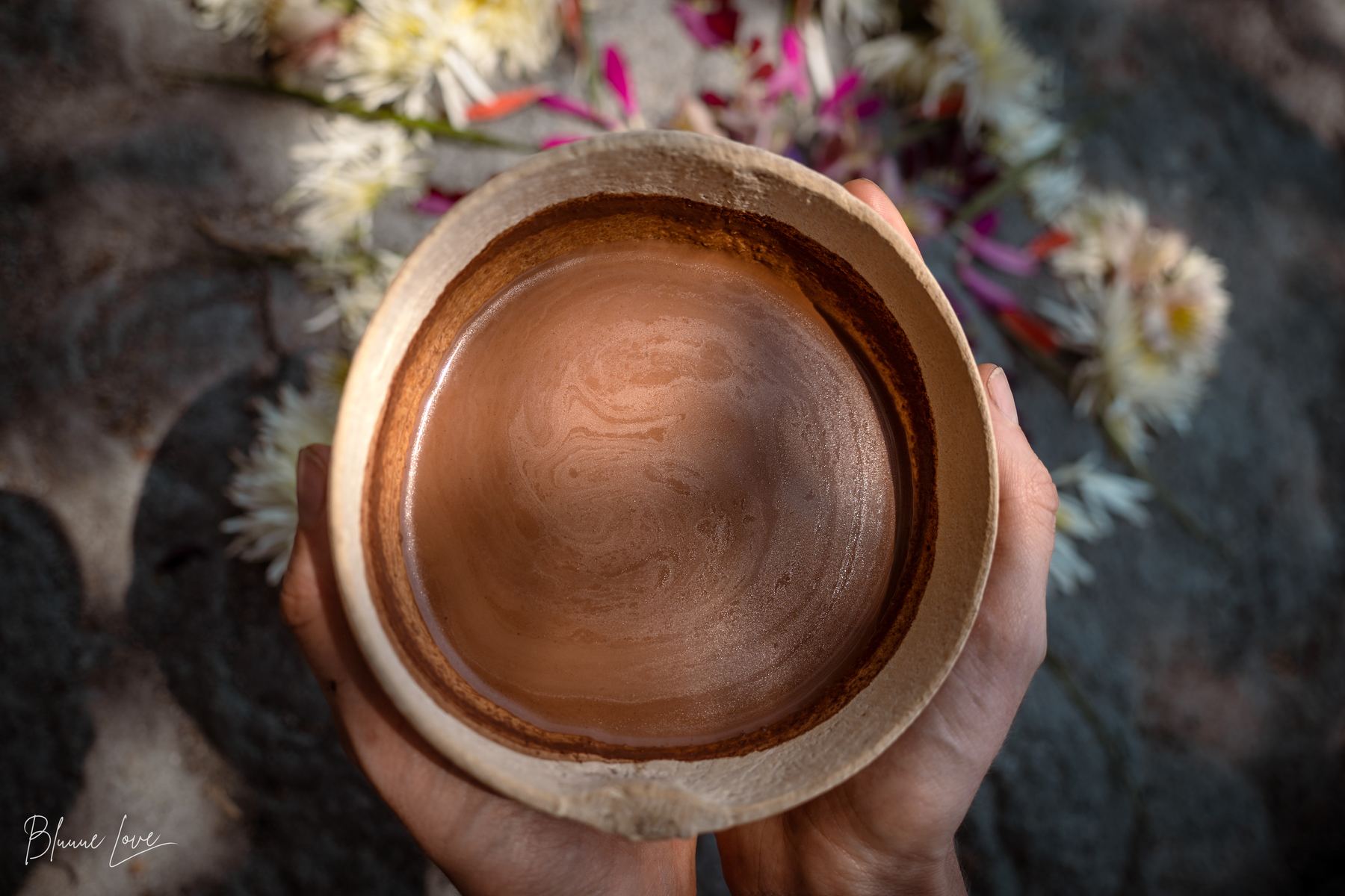 Hands holding a bowl of ceremonial cacao surrounded by flowers