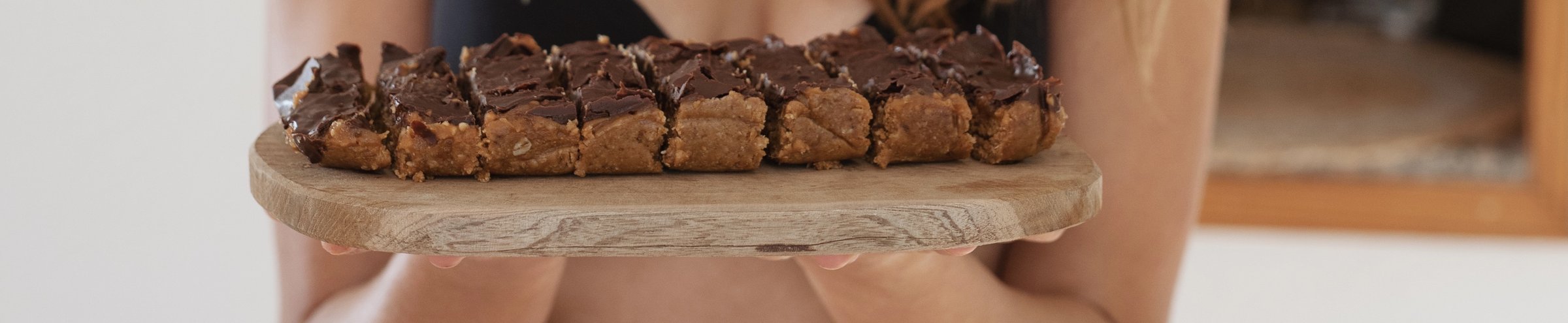 Sliced superfood snickers bars with a glossy ceremonial cacao coating, held on a wooden board